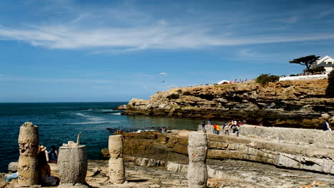 Visitors-enjoy-nice-weather-at-Hermanus-Old-Harbour,-powered-paraglider-in-air