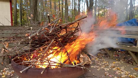 Topf-Mit-Ästen-In-Brand-In-Großem-Topf-An-Windigen-Tagen,-Während-Der-Mann-Vorne-Vorbeigeht