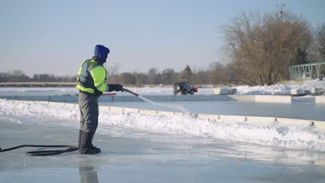 Trabajador-De-Mantenimiento-Rociando-Agua-En-Una-Pista-De-Hielo-Al-Aire-Libre,-Cámara-Lenta