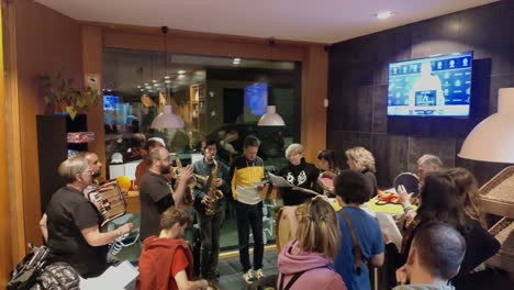 Group-of-musicians-with-men-and-women-playing-instruments-and-singing-live-in-a-bar-entertaining-customers-during-the-evening-celebration,-shooting-turning-right,-Ordes,-Galicia,-Spain