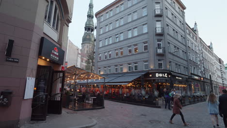 Gente-Caminando-En-La-Calle-Pasando-Por-Un-Restaurante-De-Moda-En-La-Esquina-De-La-Calle-En-Riga,-Letonia-Al-Atardecer