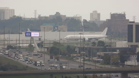 Traffic-is-moving-slowly-on-the-highway-during-rush-hour,-while-a-plane-is-driving-on-the-runway-in-the-background