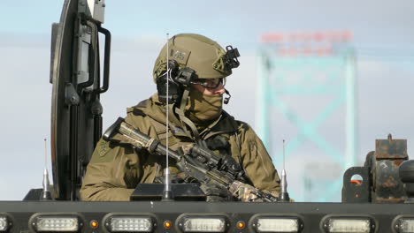 An-alert-officer-from-the-Royal-Canadian-Mounted-Police-dressed-in-full-tactical-combat-gear-standing-out-of-the-roof-of-an-armoured-vehicle-during-the-Freedom-Day-Rally,-Windsor,-Ontario,-Canada