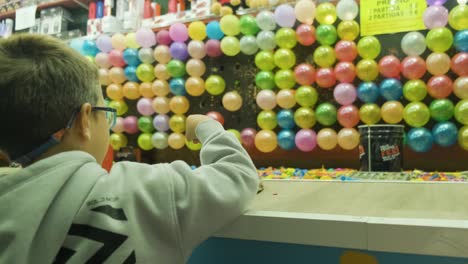 Kleiner-Junge-Wirft-Darts-Zu-Bunte-Luftballons-Beim-Karneval-Von-San-Froilán,-Stadt-Lugo,-Von-Hinten-Erschossen