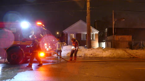 Un-Equipo-De-Bomberos-Se-Acurrucó-Alrededor-De-La-Parte-Delantera-De-Un-Camión-De-Bomberos-En-La-Escena-Del-Incendio-De-Una-Casa-Residencial-Por-La-Noche,-Toronto,-Canadá