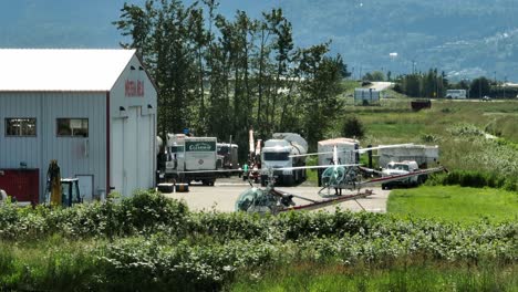 Helicóptero-Girando-Su-Rotor-Estacionado-En-El-Aeropuerto-Chiliwack-Con-Vehículos-En-El-Fondo-En-Canadá