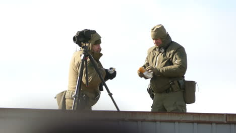 Dos-Policías-En-Uniforme-De-Invierno-Comiendo-Su-Comida-Durante-El-Descanso-Junto-Al-Trípode-De-La-Cámara-En-Ontario,-Canadá