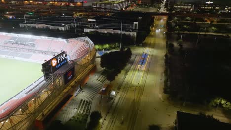 Aerial-view-passing-the-PNC-Stadium-towards-the-Houston-skyline,-nighttime-in-Texas,-USA---tilt,-drone-shot