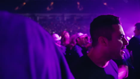 Spectators-Crowd-Jostle-Dance-and-Sing-During-Indoor-Arena-Music-Concert-Show,-Colorful-Spotlights-Excited-Jostling-People-and-Audience-Stands-Around