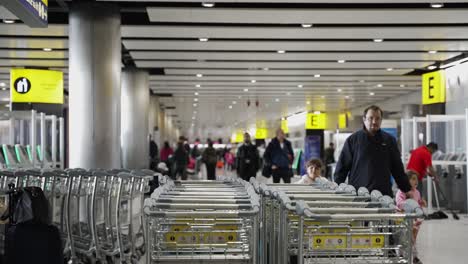 Fila-De-Carros-De-Equipaje-Dentro-De-La-Terminal-3-Del-Aeropuerto-De-Heathrow-Con-Gente-Pasando