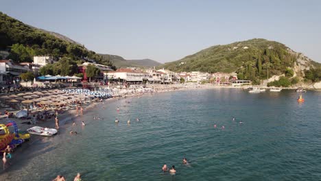 Aerial-over-popular-Valtos-beach,-Parga---people-swimming,-sunbathers,-parasols