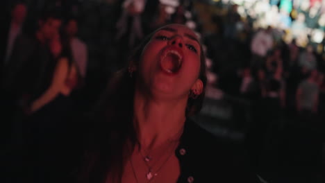 Joyful-Young-Woman-Lady-Spectator-Cheering-Singing-and-Dancing-During-Music-Show,-Indoor-Portrait-with-Spotlights-and-Audience-Crowd-Behind-Her