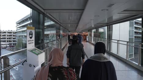 POV-Shot-Of-Family-Making-Their-Way-Through-To-Terminal-T3-Car-Park-At-Heathrow-Airport,-Crossing-Over-Gangway-Bridge