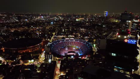 Vista-Aérea-Alrededor-De-La-Sede-De-La-Ciudad-De-Los-Deportes,-Parpadeando-Durante-La-Noche-Del-Concierto-En-La-Ciudad-De-México---Dando-Vueltas,-Tiro-De-Drones