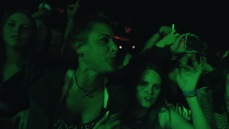 Joven-Dama-Frente-Al-Escenario-Animando-El-Canto-Durante-El-Concierto-De-Música,-Focos-Coloridos-Y-Damas-Espectadoras-Se-Aglomeran,-Jóvenes-Y-Entretenimiento