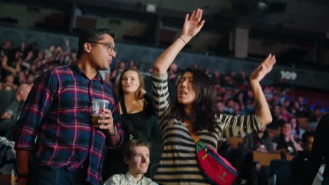 Mujer-Joven-En-La-Arena-Se-Pone-A-Bailar-Con-Los-Brazos-Levantados-Y-Las-Manos-Arriba-Durante-El-Concierto-De-Música,-El-Novio-A-Su-Lado-Y-Los-Espectadores-Alrededor