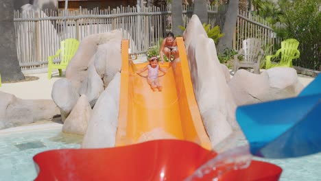 Mamá-Ayudando-A-Su-Pequeña-Hija-A-Salir-Del-Tobogán-En-La-Piscina