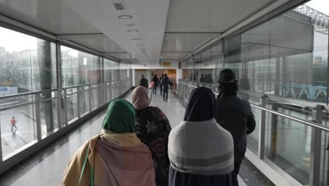 POV-Shot-Behind-Family-Making-Their-Way-Through-To-Departures-Terminal-T3-At-Heathrow-Airport,-Crossing-Over-Gangway-Bridge