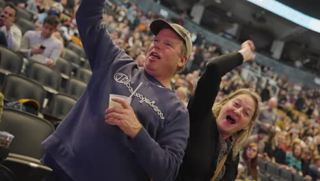 Alegre-Pareja-De-Mediana-Edad-Espectadores-Fanáticos-Bailando-Brazos-Arriba-Sosteniendo-Una-Copa-De-Bebida-Durante-El-Concierto-De-Música,-Disfrutando-Del-Evento,-Los-Puestos-De-Arena-Y-La-Multitud-De-La-Audiencia-Alrededor