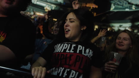 Alegre-Y-Emocionada-Mujer-Joven-Animando-A-Cantar-Bailando-Y-Saltando-Durante-Un-Concierto-De-Música,-Focos-Coloridos-Y-Espectadores-Agolpados-Alrededor,-Jóvenes-Y-Entretenimiento