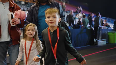 Joyful-Boy-and-Girl-Kids-With-Dads-Dancing-in-Arena-During-Music-Concert-Show,-Spectators-Crowd-in-Stands-in-Background