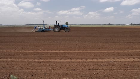 Farmer-runs-behind-planter-pulled-by-seeding-tractor-in-field-soil