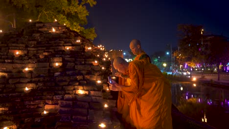 Zwei-Junge-Thailändische-Mönche-In-Orangefarbenen-Gewändern,-Die-Während-Des-Yi-Peng-Festivals-Kerzen-Fotografieren