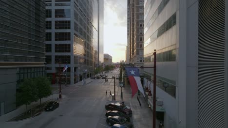 Street-level-Aerial-view-of-parked-cars-and-a-flag-on-Texas-avenue-in-Houston-city---rising,-pull-back,-drone-shot