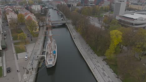 An-aerial-view-The-masted-sailing-ship-Meridian,-a-symbol-of-Klaipda,-is-moored-at-the-Danes-River-quays-in-Klaipeda-city