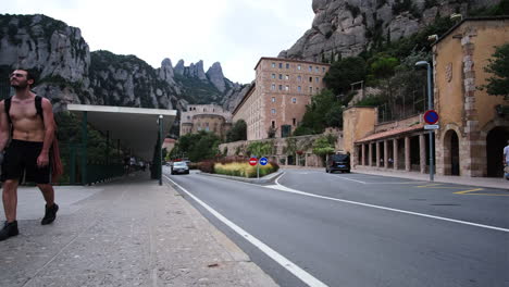 Blick-Auf-Das-Kloster-Montserrat-Von-Der-Straße-Aus-Mit-2-Männern,-Die-Auf-Der-Straße-Laufen