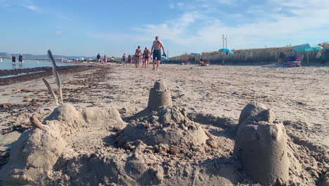 Castillos-De-Arena-Y-Figuras-De-Arena-Con-Gente-Caminando-En-El-Fondo