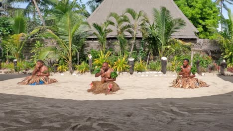 Bailarines-Fiyianos-Masculinos-Sentados-En-La-Arena-Con-Faldas-De-Hierba-Realizando-Fiji