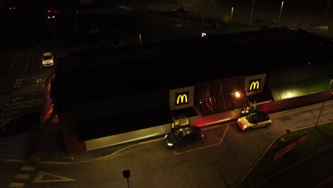 Cola-De-Autos-En-La-Comida-Rápida-De-Mcdonalds-En-Coche-Por-La-Noche-En-La-Vista-Aérea-De-La-Ciudad-Del-Norte-Del-Reino-Unido