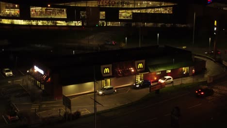 Cola-De-Coches-Fuera-De-La-Comida-Rápida-De-Mcdonalds-En-Coche-Iluminado-Por-La-Noche-En-La-Vista-Orbital-Aérea-De-La-Ciudad-Del-Norte-Del-Reino-Unido