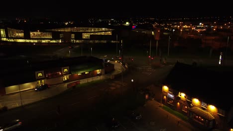 Volando-Sobre-La-Unidad-De-Comida-Rápida-Mcdonalds-Iluminada-Por-La-Noche-Junto-A-La-Vista-Aérea-De-La-Autopista-De-La-Ciudad-Del-Reino-Unido-Descendiendo-A-La-Izquierda