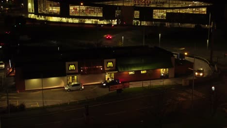 Cola-De-Vehículos-Fuera-De-La-Unidad-De-Comida-Rápida-Mcdonalds-Iluminada-Por-La-Noche-En-La-Vista-Orbital-Aérea-De-La-Ciudad-Del-Norte-Del-Reino-Unido