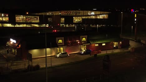 Vehículos-Que-Esperan-Fuera-De-La-Unidad-De-Comida-Rápida-Mcdonalds-Iluminada-Por-La-Noche-En-La-Vista-Orbital-Aérea-De-La-Ciudad-Del-Norte-Del-Reino-Unido