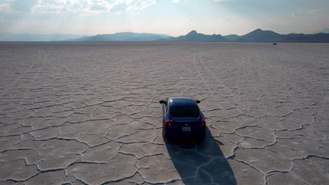 Luftaufnahme-Eines-Autos,-Das-Während-Eines-Sonnigen-Tages-Auf-Einem-Endlosen,-Rissigen,-Trockenen-Bettsee-In-Utah,-USA,-Fährt