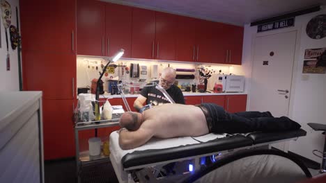 Tattoo-artist-tatooing-his-client-who-is-laying-on-the-table-in-his-studio