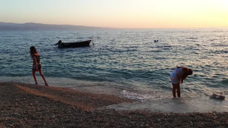 Niños-Corriendo-Por-El-Agua-En-El-Mar-Al-Atardecer,-Retroiluminados