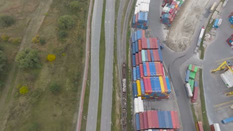 El-Tren-De-Vista-Aérea-Tira-De-Vagones-Con-Carga-Paralela-A-La-Carretera-Del-Automóvil-Y-La-Terminal-De-Carga-En-La-Ciudad-De-Klaipeda