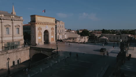 View-Of-Cars-Driving-And-People-Passing-By-Arc-de-Triomphe-In-Montpellier,-France-On-A-Sunny-Day