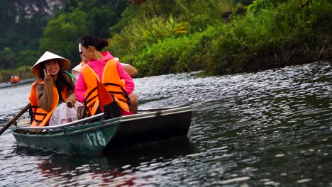 Angled-Shot-Of-Tourist-In-Orange-Life-Jacket-Posing-With-V-Sign-On-Boat-Ride-Along-River