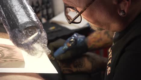 Artista-Del-Tatuaje-Coloreando-El-Brazo-Con-La-Aguja-De-La-Pistola-Del-Tatuaje