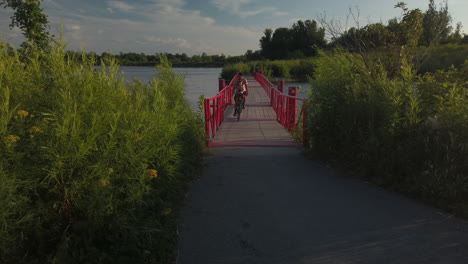 Weite-Außenaufnahme-Des-Fahrradduos,-Das-Die-Rote-Schwimmbrücke-Im-Tommy-Thompson-Park-überquert