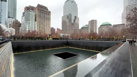 Zona-Cero-En-El-Memorial-Y-Museo-Nacional-Del-11-De-Septiembre-911-Memorial-Y-Museo---Inclínate-Hacia-Arriba-Para-Revelar-El-Horizonte-De-La-Ciudad-De-Nueva-York-En-Un-Día-Lluvioso-Y-Nublado