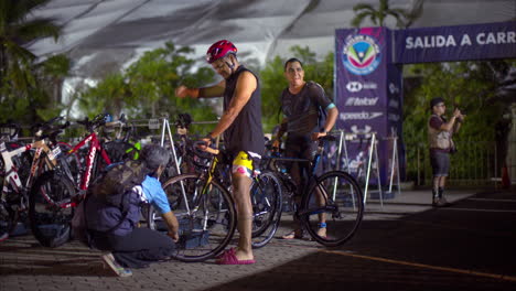 Athlet,-Der-Seine-Fahrradreifen-Inspiziert,-Bevor-Der-Triathlon-Wettkampf-Beginnt,-Trägt-Badebekleidung-Und-Helm