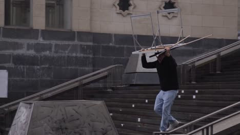 Man-with-a-table-on-his-head-running-down-the-stairs-of-Monts-des-Arts-in-Brussels,-Belgium