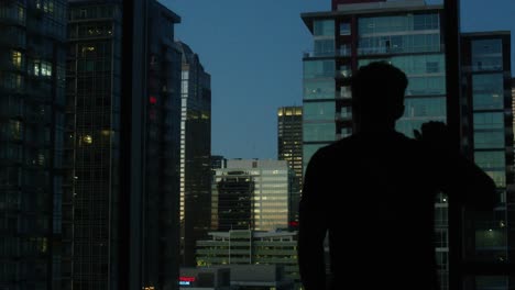 Mann-In-Tiefen-Gedanken-Mit-Blick-Auf-Die-Stadt-Mit-Wolkenkratzern,-Während-Der-Blauen-Stunde-In-Der-Abenddämmerung