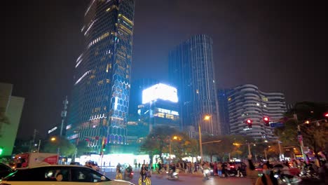 Sanlitun-Road-Peking-4k---Belebte-Nachtstraße-Mit-Leuten,-Die-Fahrräder-Fahren-Und-Die-Straßen-überqueren,-Und-Wunderschönem-Skylinenhintergrund